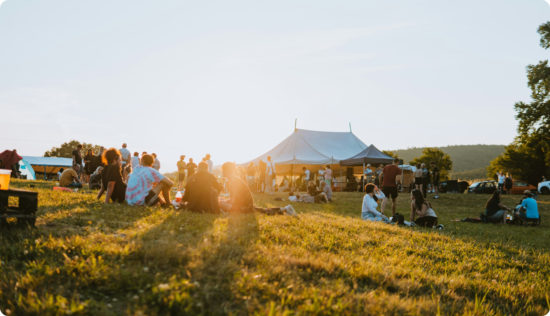 Festivaliers profitant d'un coucher de soleil dans un champ avec un grand chapiteau en arrière-plan